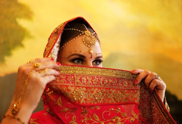 Beautiful indian bride. Young hindu woman model with traditional jewelry. Indian costume red saree. Indian or Muslim woman covers her face.