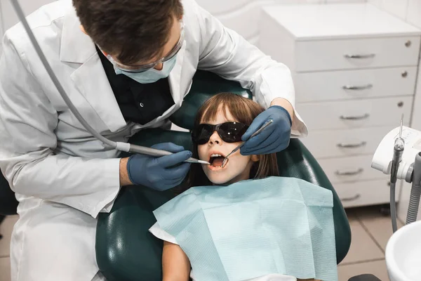 People, medicine, stomatology, technology and health care concept. Professional young male dentist working with little girl in clinic.