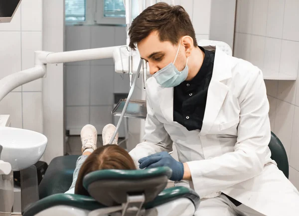 People, medicine, stomatology, technology and health care concept. Professional young male dentist working with little girl in clinic.