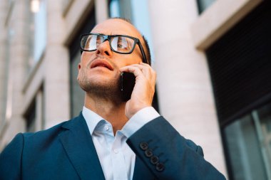 Business, people, tehnology and lifestyle concept: Happy businessman using modern smartphone near office, successful employer to make a deal while standing office.