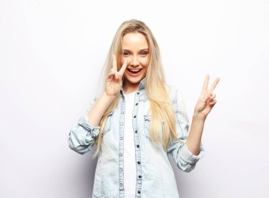 charming young woman with long blond hair wearing casual denim shirt smiling and show victory sign over white background