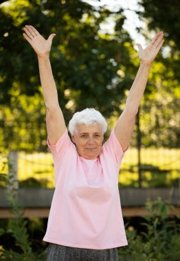 Elderly woman with short hair practicing yoga and tai chi outdoors. Old female meditating.