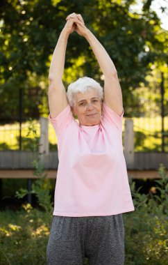 Elderly woman with short hair practicing yoga and tai chi outdoors. Old female meditating.