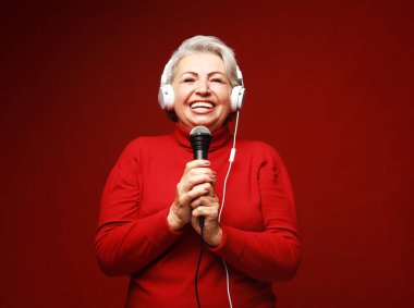 Emotion, lifestyle and old people concept: Happy senior woman singing with microphone, having fun, expressing musical talent over red background