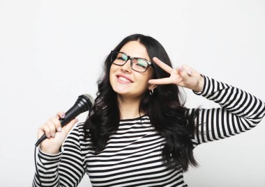 Young brunette curvy woman singer with a microphone over light grey background
