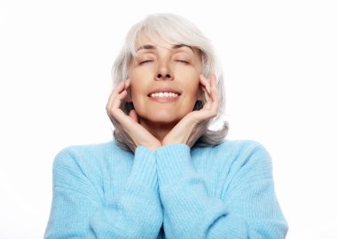 Mavi süveter giyen mutlu yaşlı kadın beyaz arka planda gülümsüyor.