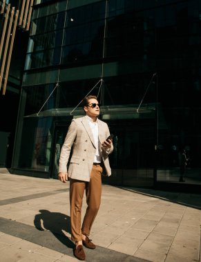 Handsome young businessman while walking outdoors with office building in the background. Summer day.