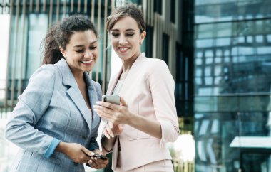 Business, people, tehnology and lifestyle concept: Two business women with mobiles near office. Summer day.