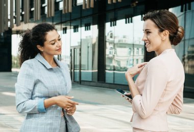 Two business women having a casual meeting or discussion near a modern office. Summer time.