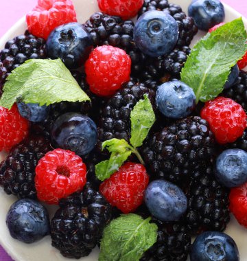 Yaprakla böğürtlen karıştır. Beyaz arka planda izole edilmiş çeşitli taze meyveler. Ahududu, yabanmersini, kızılcık, böğürtlen ve nane yaprakları