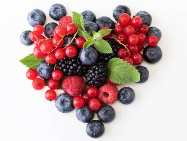 Kalp şeklinde yaprakla böğürtlenleri karıştır. Beyaz arka planda izole edilmiş çeşitli taze meyveler. Ahududu, yabanmersini, kızılcık, böğürtlen ve nane yaprakları.