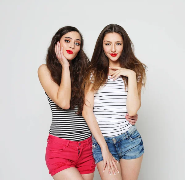 lifestyle, emotion and people concept: Two young female friends standing together and having fun. Looking at camera. Portrait over grey background.