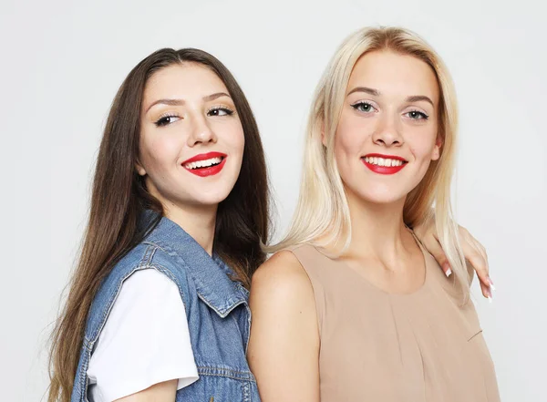 lifestyle, emotion and people concept: Two young female friends standing together and having fun. Looking at camera. Portrait over grey background.