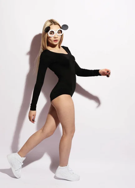 Beautiful young woman model in a gymnastic bodysuit and sunglasses posing on a white background. Full length portrait.