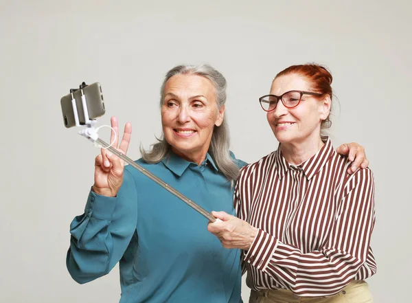 两个年长的妇女朋友拿着一根用灰色背景隔离的棍子自拍 技术和老年人概念 — 图库照片
