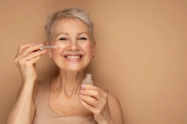 Ευτυχισμένη Ηλικιωμένη Κυρία Εφαρμόζει Καλλυντικό Ορό Πετρελαίου Στο Πρόσωπο Φροντίζει — Φωτογραφία Αρχείου
