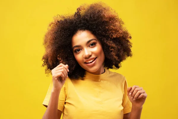 Positive dark skinned woman dances carefree raises arms moves with rhythm of favorite music dressed casually isolated over yellow background.