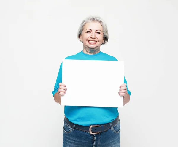 有空白广告牌或复制空间的老年妇女 穿着蓝色T恤的漂亮而有表现力的祖母的画像 工作室拍摄 孤立在灰色背景 靠近点 — 图库照片
