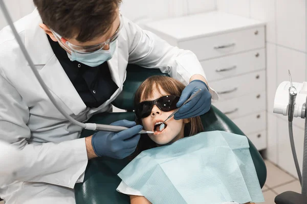 People, medicine, stomatology, technology and health care concept. Male dentist working with little girl in clinic. Close up.
