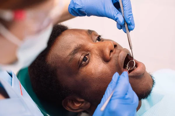 People, medicine, stomatology, technology and health care concept. Portrait of black male patient getting teeth treatment with dentist at modern clinic.