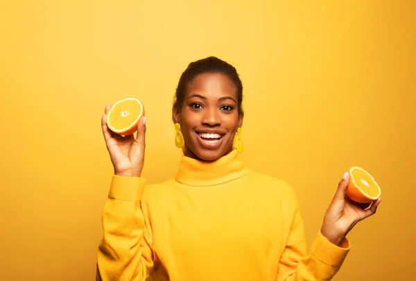 若い幸せなアフロアメリカ人女性は黄色の背景に隔離された見事なオレンジ色のスライスを保持 — ストック写真