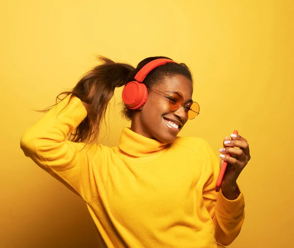 stock image Young afro american female with dances in rhythm of melody. Portrait woman with headphones over yellow color background.