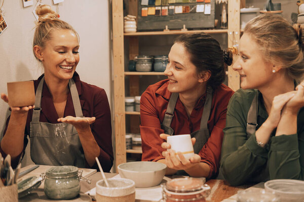 A company of three pretty young women friends make ceramic mugs in a pottery workshop. Have fun doing art.