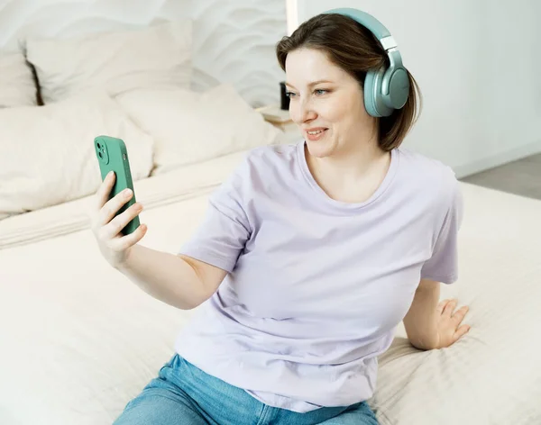 Χαμογελαστή Ενήλικη Γυναίκα Που Κάθεται Στο Κρεβάτι Ακουστικά Και Ακούει — Φωτογραφία Αρχείου
