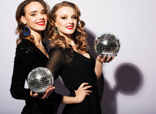 lifestyle, party and people concept: Two Young pretty women wearing black dress, holding a disco balls over grey background