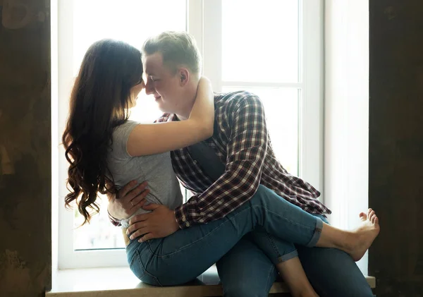 生活方式 爱情和人的观念 年轻夫妇坐在窗边的窗台上拥抱和亲吻 — 图库照片