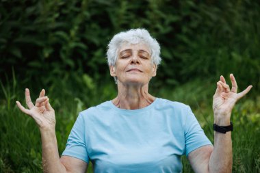 Kısa saçlı, yoga ve açık havada tai chi yapan yaşlı bir kadın. Yaşlı kadın yaz parkında meditasyon yapıyor..