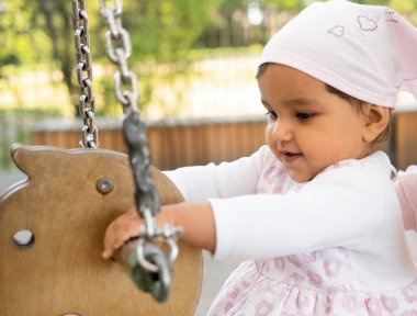 Küçük gülümseyen kız bir yaz günü parkta salıncakta oturur, oyun zamanı, mutlu yaz.