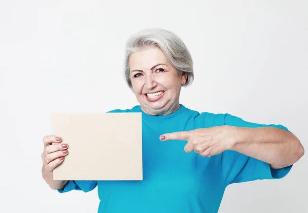 一位快乐而迷人的老妇人手里拿着一张空白的纸 用手指指着它 在白色背景下被隔离 — 图库照片