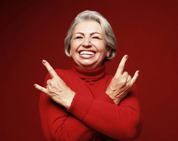 老婦人は笑い カメラで岩の標識を示しています 感情や感情 赤を背景にした表情豊かな祖母の肖像 — ストック写真