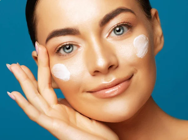 stock image Close up beauty portrait of woman applying face cream and looking away isolated over blue color background