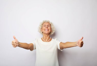 Yaşam tarzı, duygu ve yaşlılar konsepti: iyi ruh hali mutlu gülümseyen yaşlı kadın beyaz arkaplan üzerinde izole edilmiş v-işareti gösteriyor