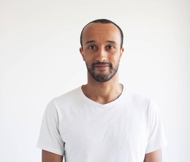 Açık gri arka planda beyaz tişört giyen traşsız genç bir adam. Afrikalı Amerikalı.