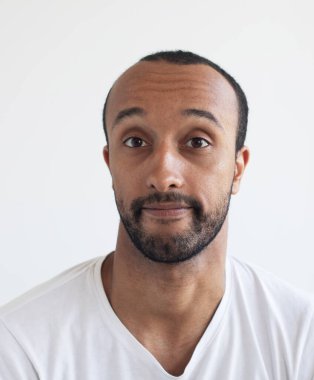 Açık gri arka planda beyaz tişört giyen traşsız genç bir adam. Afrikalı Amerikalı.