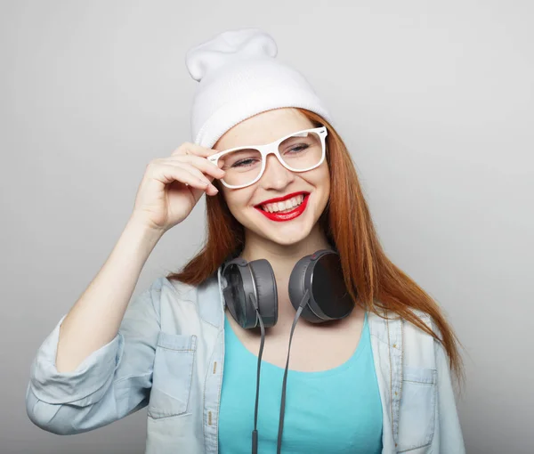 头戴白帽 头戴耳机 红头发 快乐的年轻女子 在灰蒙蒙的背景上微笑和摆姿势 — 图库照片