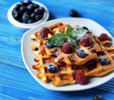 Kahvaltıda mavi ahşap masada yaban mersinli waffle ve ahududu. Kapat..