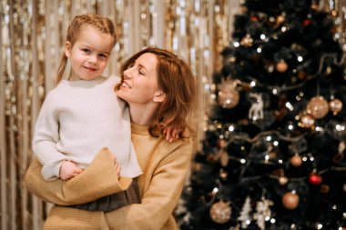 Genç bir anne, Noel ağacının yanında gülen bir kızı kollarında tutar. Aile, kış tatili ve insanlar konsepti. Mutlu zamanlar..