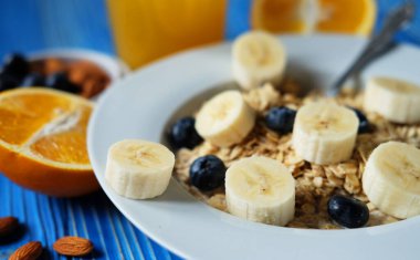 Taze böğürtlenli yulaf ezmesi, beyaz tabakta muz portakal suyu, mavi ahşap arka plan. İyi kahvaltı..