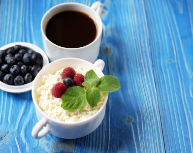 Süzme peynir ve böğürtlenler bir kase içinde bir fincan kahveyle birlikte masada. İyi kahvaltı.
