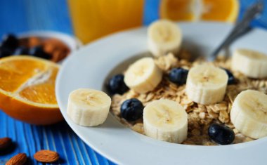 Taze böğürtlenli yulaf ezmesi, beyaz tabakta muz portakal suyu, mavi ahşap arka plan. İyi kahvaltı..
