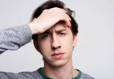 Genç bir adam baş ağrısı çekiyor. Yorgunluk, stres, depresyon. Gri arkaplanda portre.
