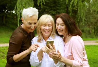 Charming old women laugh merrily and look at the screens of smartphone. Having fun in retirement on a summer afternoon. Golden age.