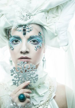 Parti, noel ve halk konsepti: Yeni yıl tarzında yaratıcı makyajlı genç güzel bir kadın yüzünde gümüş kar taneleri tutuyor. Kar Kraliçesi, peri.