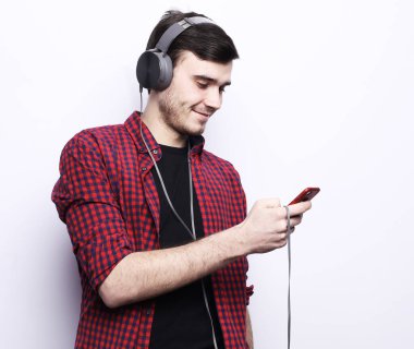 Gülümseyen yakışıklı erkek model bir sandalyeye oturur ve kulaklıkla müzik dinler, beyaz arka planda bir portre. Yaşam tarzı ve insan kavramı.