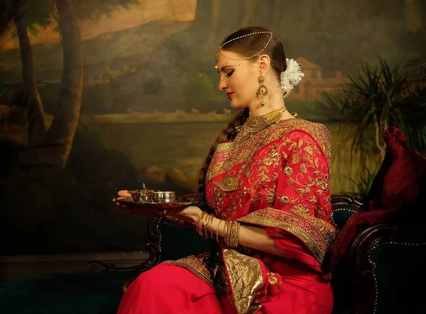 迷人的印度新娘 身穿印度教红色传统婚纱 绣有黄金 坐在花边的沙发上 微笑着 手持小金盒 — 图库照片