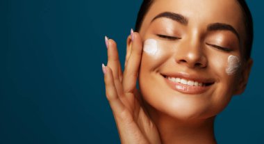 Güzel bir genç kadının yüz kremi sürerken ki güzel portresini kapat. Kapalı gözlü bir kadın model.